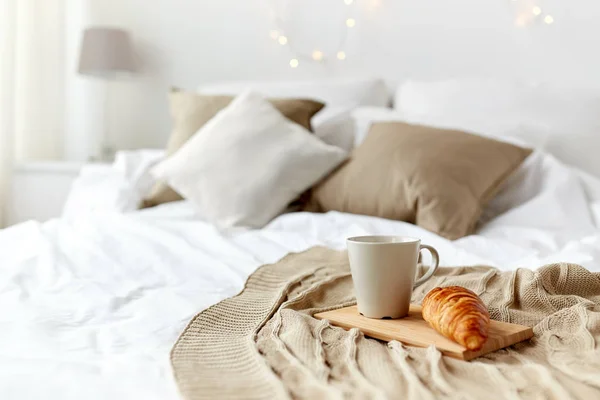 Taza de café y croissant a cuadros en la cama en casa —  Fotos de Stock