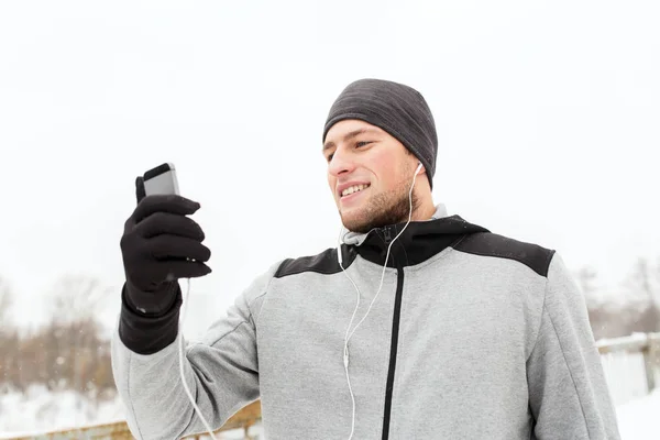 Счастливый человек с наушниками и смартфоном зимой — стоковое фото