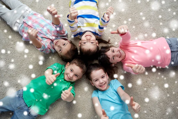 Niños felices tumbados en el suelo y mostrando los pulgares hacia arriba —  Fotos de Stock