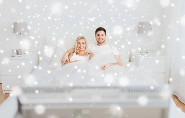 Happy couple lying in bed at home and watching tv — Stock Photo, Image
