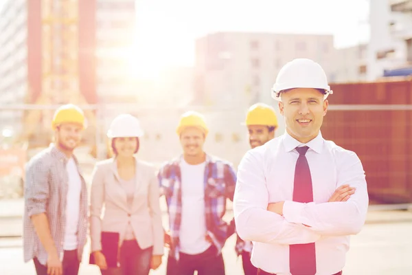 Grupp av leende byggare i hardhats utomhus — Stockfoto