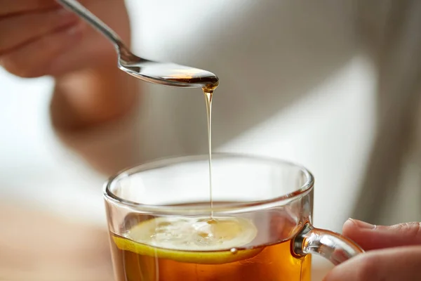 Close up of woman adding honey to tea with lemon — Stock Photo, Image