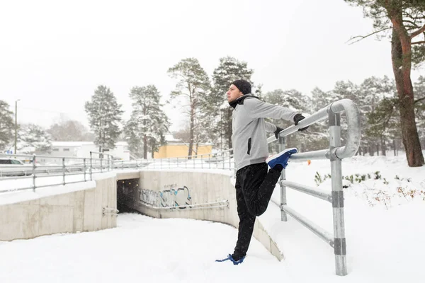 sports man stretching leg at fence in winter