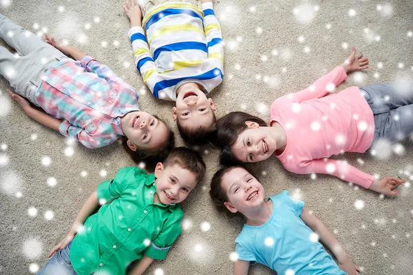 Happy smiling children lying on floor over snow — Stock Photo, Image
