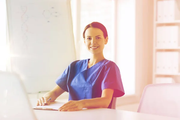 Happy female doctor or nurse writing to clipboard — Stock Photo, Image