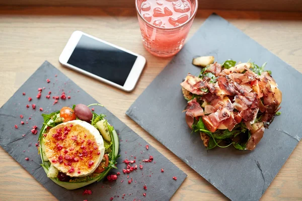 Queijo de cabra e saladas de presunto com smartphone no café — Fotografia de Stock