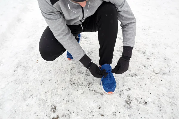 Man with earphones tying sports shoes in winter — Stock Photo, Image