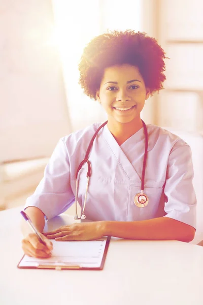 Happy female doctor or nurse writing to clipboard — Stock Photo, Image