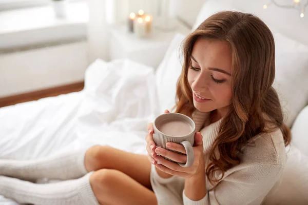 Mujer feliz con taza de cacao en la cama en casa —  Fotos de Stock