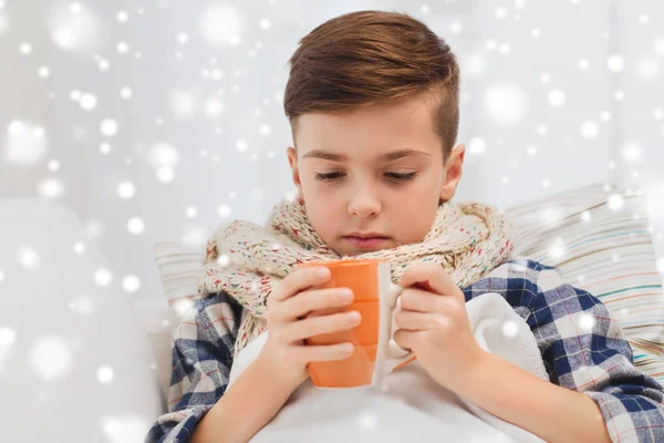 Ill boy with flu in scarf drinking tea at home — Stock Photo, Image