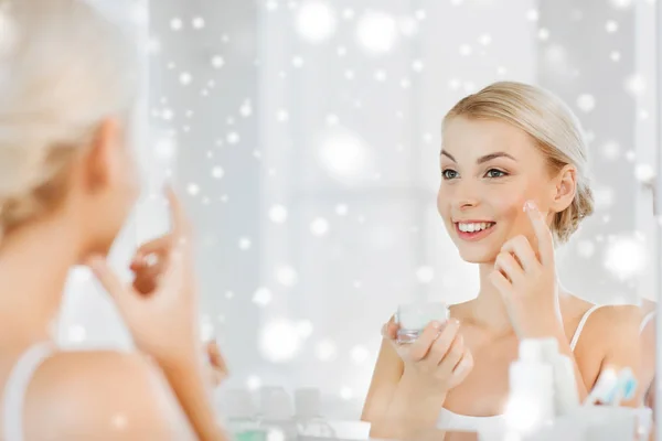 Счастливая женщина наносит крем на лицо в ванной комнате — стоковое фото