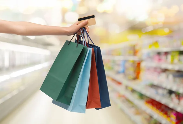 Main avec sacs à provisions et carte de crédit en magasin — Photo