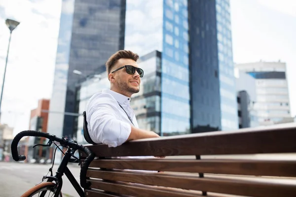 Felice giovane uomo con la bicicletta seduto sulla panchina della città — Foto Stock