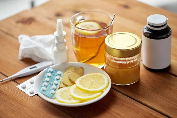 Medicamentos, termómetro, miel y taza de té sobre madera — Foto de Stock