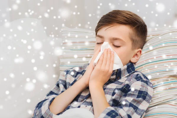 Kranker Junge liegt im Bett und pustet sich zu Hause die Nase aus — Stockfoto