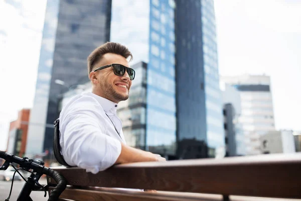 Glücklicher junger Mann mit Fahrrad sitzt auf Stadtbank — Stockfoto
