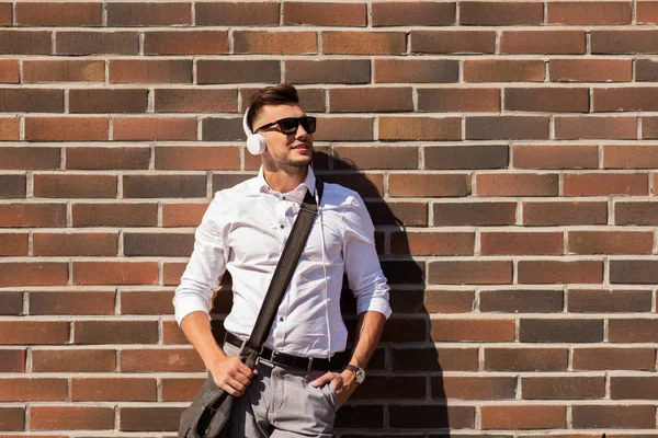 Ung mann i hodetelefoner med pose over murveggen – stockfoto