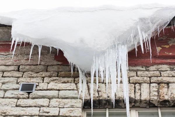 Сосульки и снег свисают с крыши здания — стоковое фото