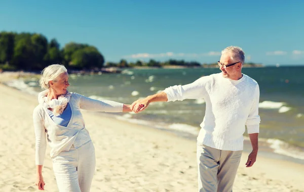 Счастливая пожилая пара, держащаяся за руки на летнем пляже — стоковое фото