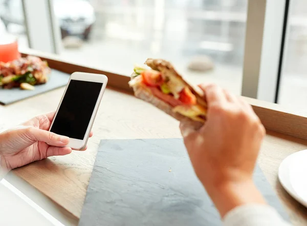 Женщина со смартфоном и сэндвичем в ресторане — стоковое фото