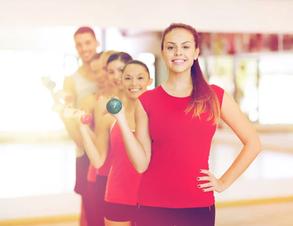 Groupe de personnes souriantes avec haltères dans la salle de gym — Photo