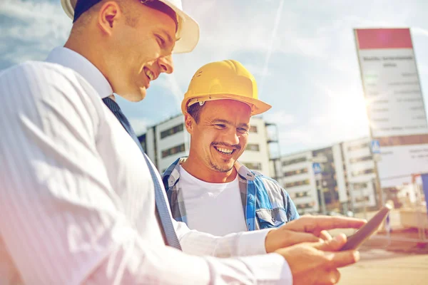 Construtores felizes em hardhats com tablet pc ao ar livre — Fotografia de Stock