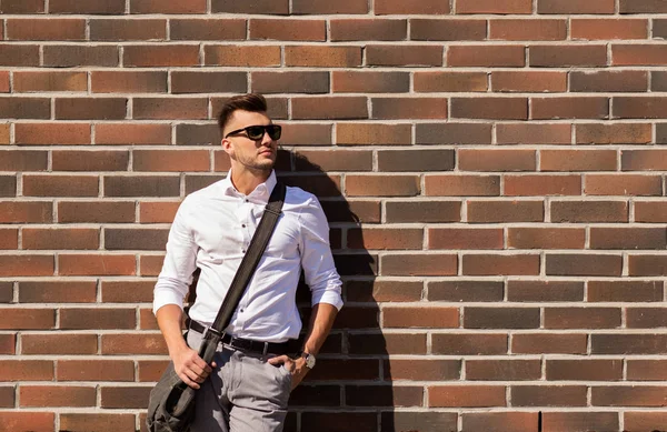 Fiatal férfi napszemüveg táska felett brickwall — Stock Fotó