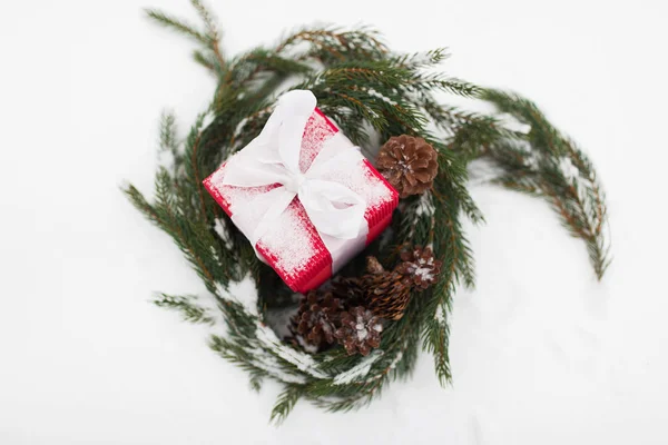 Regalo di Natale e ghirlanda di abeti con coni sulla neve — Foto Stock