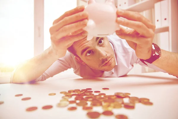 Бизнесмен с копилкой и монетами в офисе — стоковое фото
