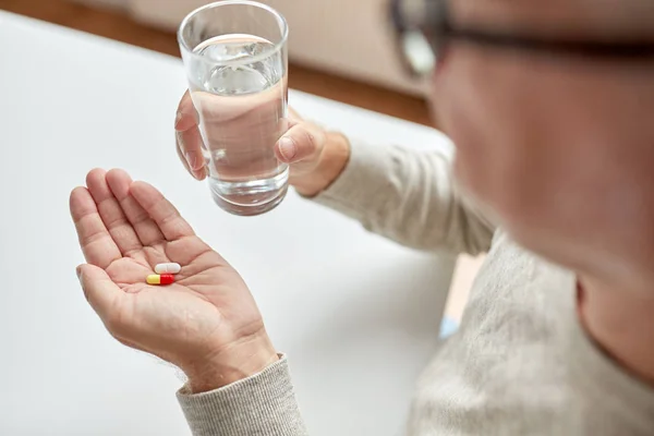 Närbild av gamla mannen händerna med piller och vatten — Stockfoto