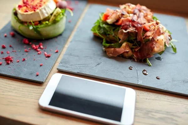 Козячий сир та салати з шинкою зі смартфоном у кафе — стокове фото