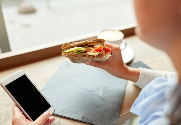 Mulher com smartphone e sanduíche no restaurante — Fotografia de Stock