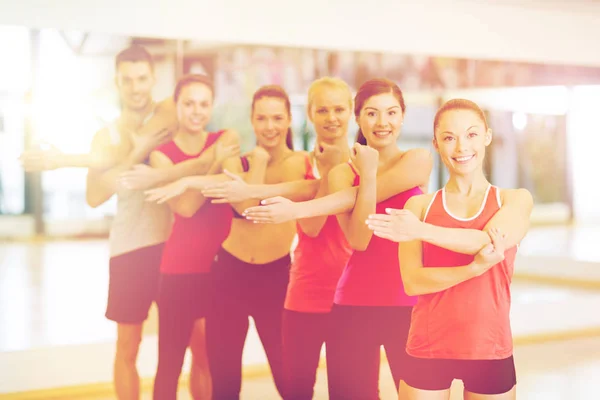 Grupo de personas sonrientes estirándose en el gimnasio — Foto de Stock