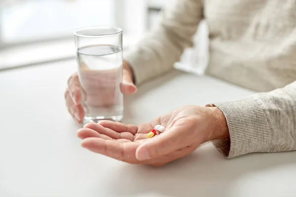 Primer plano de las manos del anciano con píldoras y agua — Foto de Stock