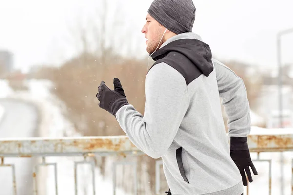 Человек в наушниках бежит вдоль зимнего моста — стоковое фото