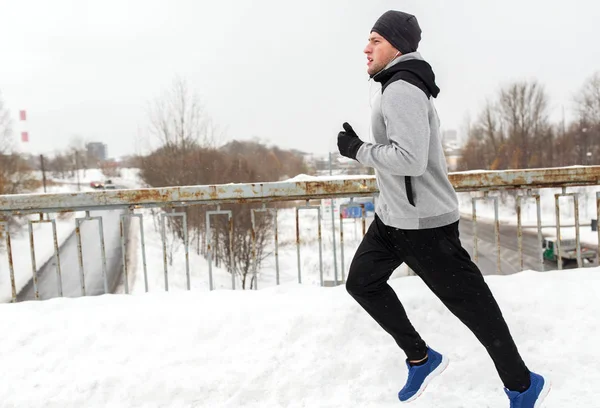 Человек в наушниках бежит вдоль зимнего моста — стоковое фото