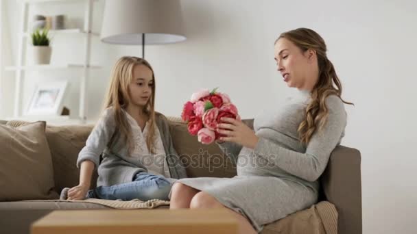 Счастливая беременная женщина с цветами и девочкой дома — стоковое видео