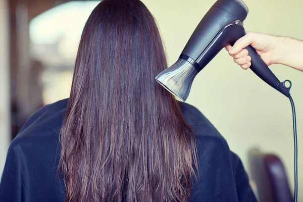 Stylista ruku s ventilátorem vysušuje vlasy žena v salonu — Stock fotografie