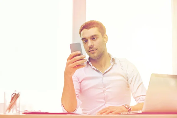 Бизнесмен со смартфоном и ноутбуком в офисе — стоковое фото