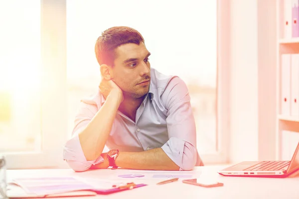 Verveeld zakenman met laptop en papieren op kantoor — Stockfoto