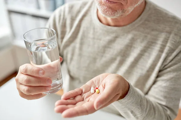 Perto de mãos de homem velho com pílulas e água — Fotografia de Stock
