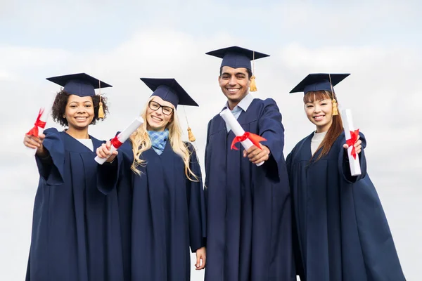 Happy students in mortar boards with diplomas — Stock Photo, Image