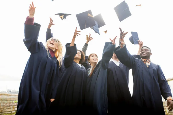 Happy students throwing mortar boards up — Stock Photo, Image