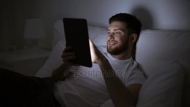 Jeune homme avec tablette PC dans le lit à la maison chambre — Video