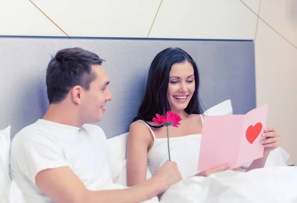 Lachende paar in bed met briefkaart en bloem — Stockfoto