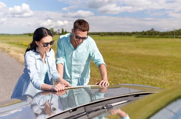 Happy man and woman with road map on car hood — Stock Photo, Image