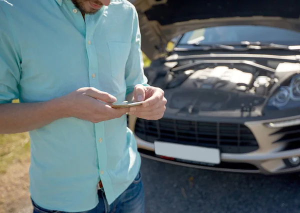 Close up de homem com smartphone e carro quebrado — Fotografia de Stock