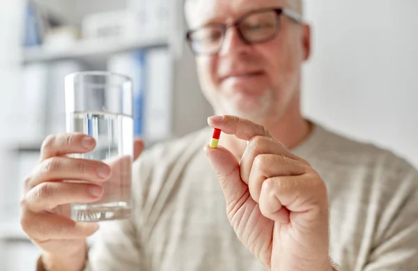 Close up de mãos de homem velho com pílula e água — Fotografia de Stock