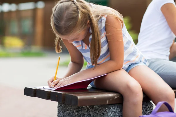 Student tjej skriver till anteckningsboken på skolgården — Stockfoto
