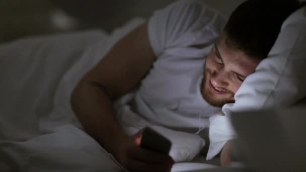 Hombre con smartphone y auriculares en la cama por la noche — Vídeo de stock